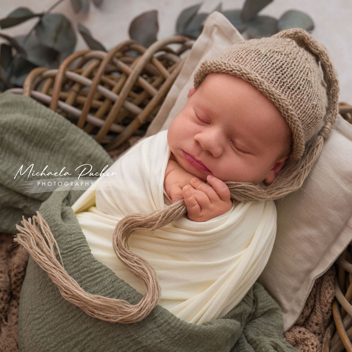 Schlafendes Neugeborenes in natürlichen Farben eingewickelt, hält die Kordel seiner Strickmütze in der Hand und liegt auf einem kleinen Kissen in einem Korb.